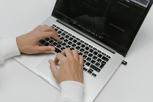 Close-up of hands typing on a laptop with a USB device on a white background. Ideal for tech and cybersecurity themes.